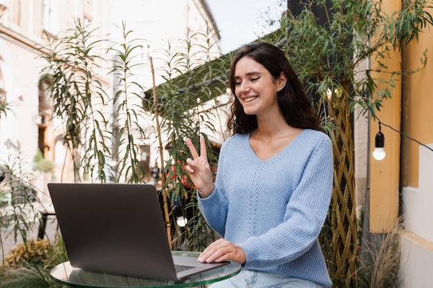 Chica alegre con una laptop haciendo muecas y chateando por video con amigos y familiares en un café al aire libre La mujer emocional sonríe y se comunica con amigos y se divierte a través de una conexión de video