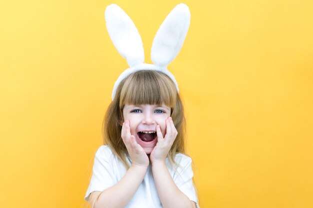 Chica alegre con orejas de conejo en la cabeza sobre un fondo amarillo Divertido niño loco feliz Niño de Pascua Preparación para las vacaciones de Pascua artículos promocionales copia espacio para maqueta de texto