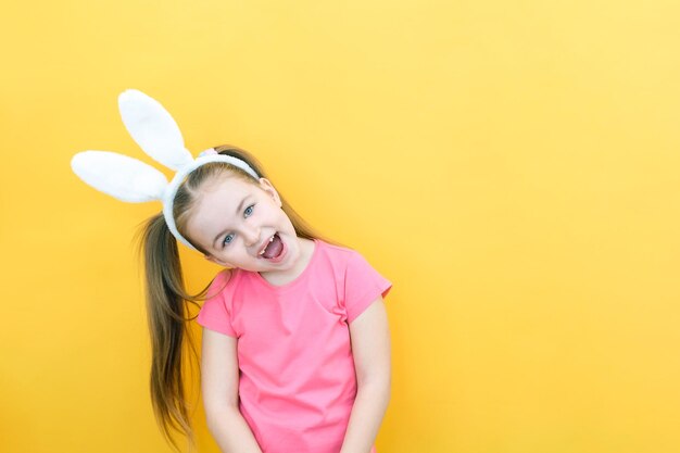 Chica alegre con orejas de conejo en la cabeza sobre un fondo amarillo Divertido niño loco feliz Niño de Pascua Preparación para las vacaciones de Pascua artículos promocionales copia espacio para maqueta de texto