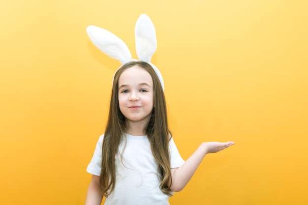 Chica alegre con orejas de conejo en la cabeza sobre un fondo amarillo Un niño feliz y divertido señala con el dedo un espacio vacío para copiar texto