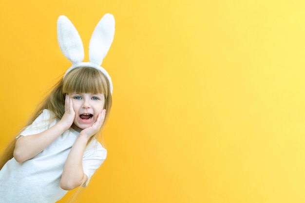 Una chica alegre con orejas de conejo en la cabeza sobre un fondo amarillo Un niño loco y feliz divertido le da un conejo Preparación para el espacio de copia de las vacaciones de Pascua para la maqueta de texto