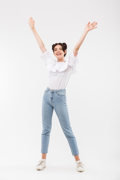 Chica alegre con peinado de bollos dobles riendo y divirtiéndose levantando los brazos, aislado en blanco