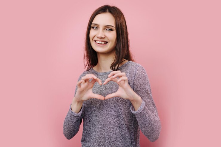 Chica alegre que muestra el signo del corazón hecho con los dedos en el estudio