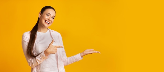 Chica alegre señalando con el dedo sosteniendo algo sobre fondo amarillo