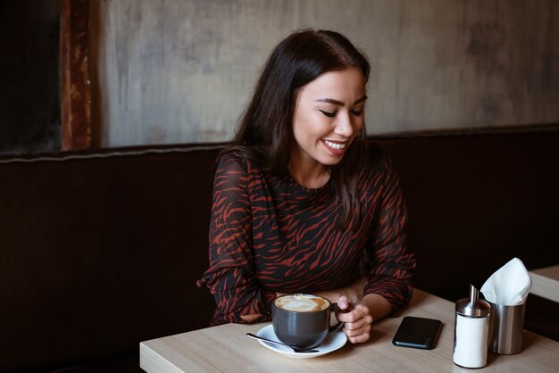 Chica alegre se sienta en una mesa en un café con una taza de café