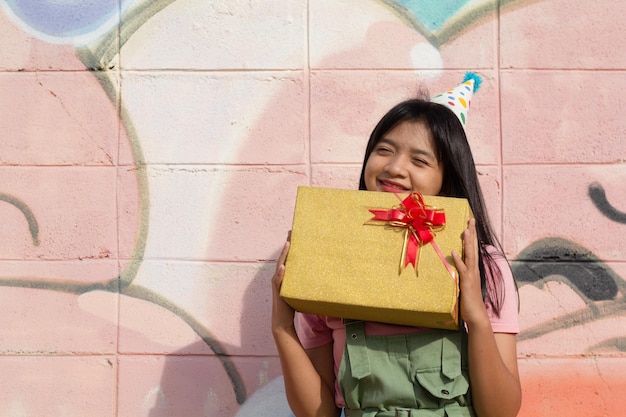 La chica alegre con sombrero de fiesta con caja de regalo sentada en un fondo colorido