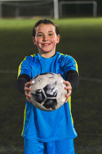 Foto chica alegre y sonriente con ropa deportiva azul sosteniendo una pelota de fútbol hacia la cámara de disparo medio