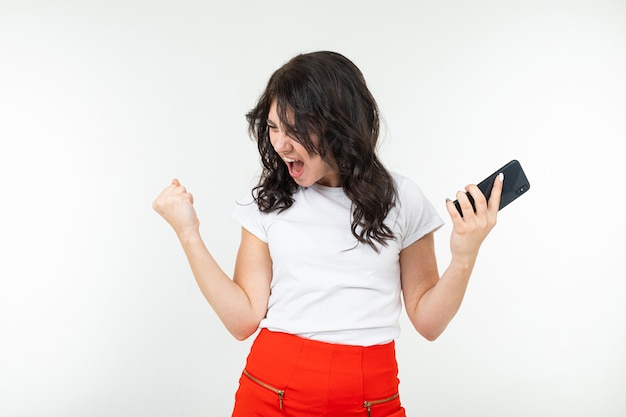 Chica alegre con un teléfono en sus manos sobre un fondo blanco con espacio de copia