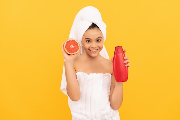 Chica alegre en toalla con botella de champú de pomelo sobre fondo amarillo