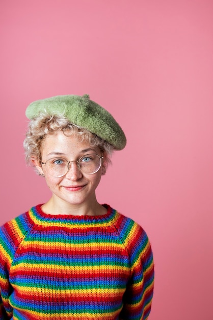 Chica alegre vestida con suéter de arco iris y boina verde en un fondo rosa