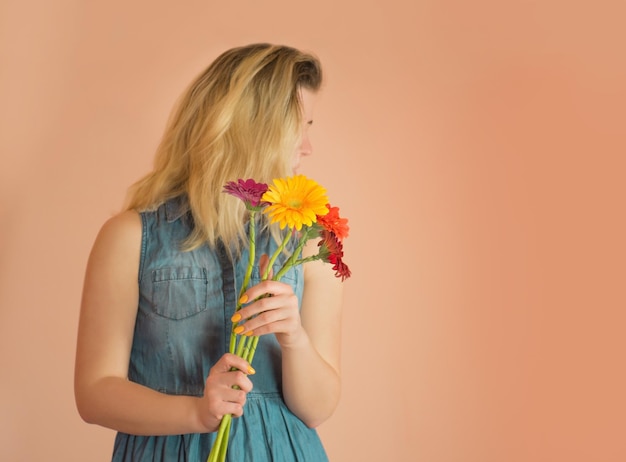 Chica alegre con vestido de mezclilla y flores de manzanilla en las manos