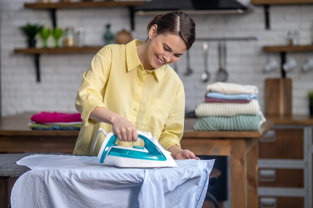 Chica alisando las arrugas de la camisa con una plancha de vapor