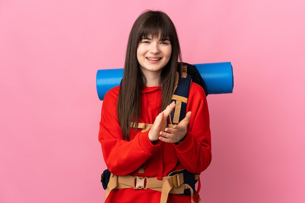 Chica alpinista con una gran mochila aislada en rosa aplaudiendo