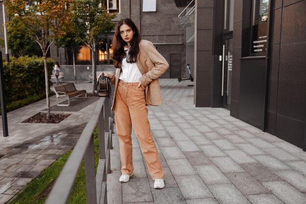 Chica alta y moderna con una chaqueta de gran tamaño se encuentra cerca de la entrada al edificio de la oficina