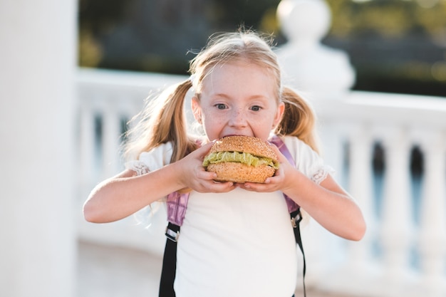 Chica alumno feliz comiendo hamburguesa al aire libre