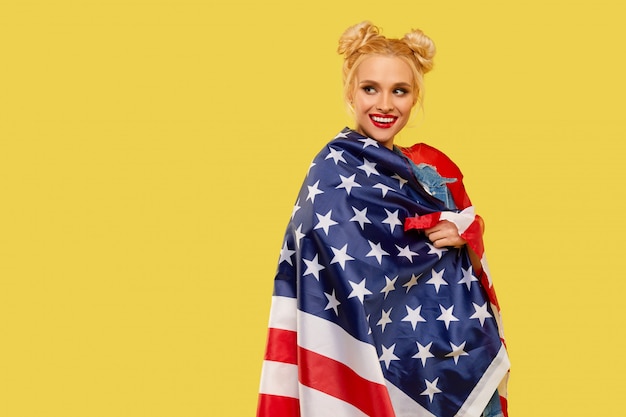 Chica americana. Feliz mujer joven en ropa de mezclilla sosteniendo la bandera de Estados Unidos aislado sobre fondo amarillo