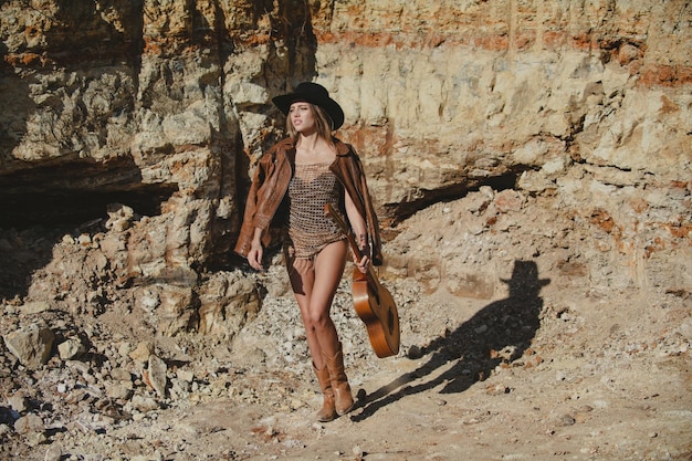 Chica americana con guitarra en estilo vaquero de vaquera de moda Mujer atractiva en traje de moda afuera Foto de moda al aire libre de una joven hermosa dama disfrutando de la primavera