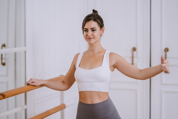 Foto chica americana morena en ropa deportiva calentándose en puestos de clase de baile en la barra de ballet hermosa