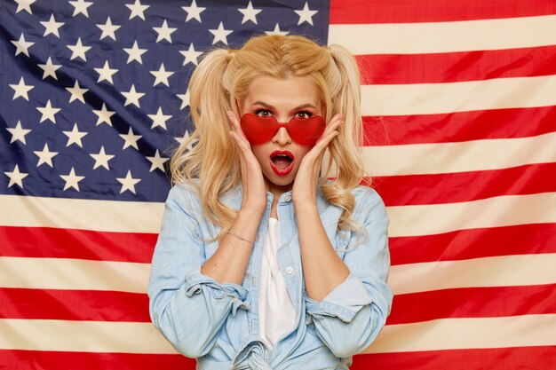 Chica americana. Retrato de feliz de joven sorprendida en el fondo de la bandera de Estados Unidos