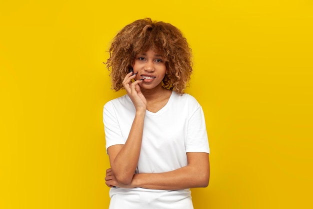 Chica americana rizada joven en camiseta blanca con sonrisas de llaves sobre fondo amarillo aislado