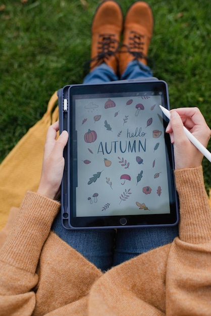 Chica anónima dibuja en una tableta gráfica en el parque, ilustraciones de otoño