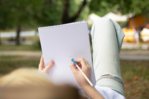 Chica anónima haciendo notas o dibujando en el libro de papel en blanco