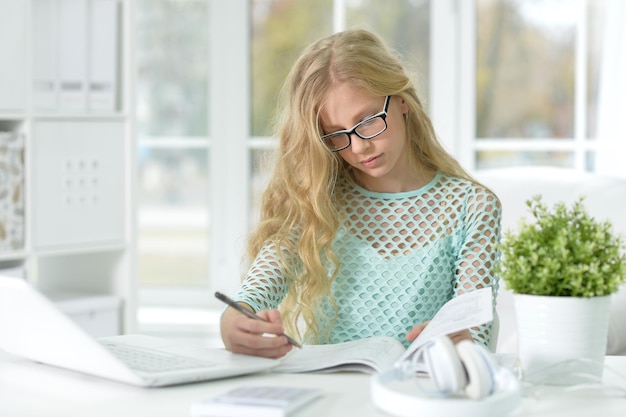 Chica con anteojos sentada en el escritorio y estudiando