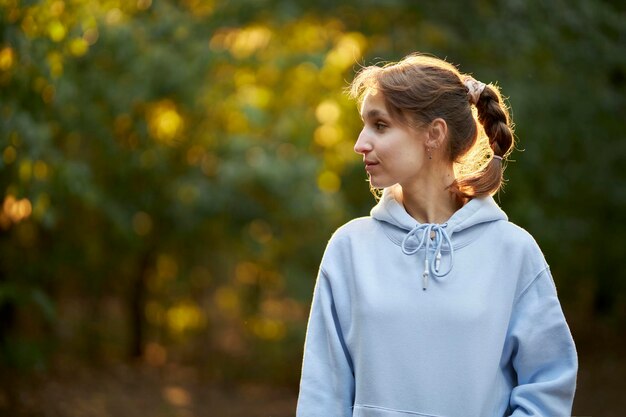 Foto una chica de apariencia europea con una capucha azul escucha música en el parque de la ciudad con auriculares