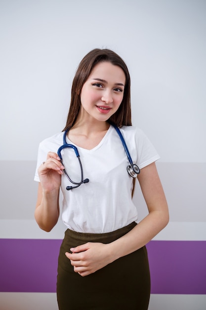 Una chica de apariencia europea con un fonendoscopio en el cuello. Sonrisas triguenas jovenes atractivas de la mujer. Ella es una joven doctora, estudiante en prácticas.