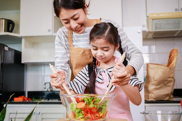 Chica aprendiendo a preparar ensalada de verduras con madre Comida saludable y divirtiéndose en la cocina en casa