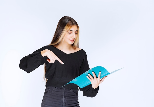 Chica apuntando a algo en la carpeta azul. Foto de alta calidad