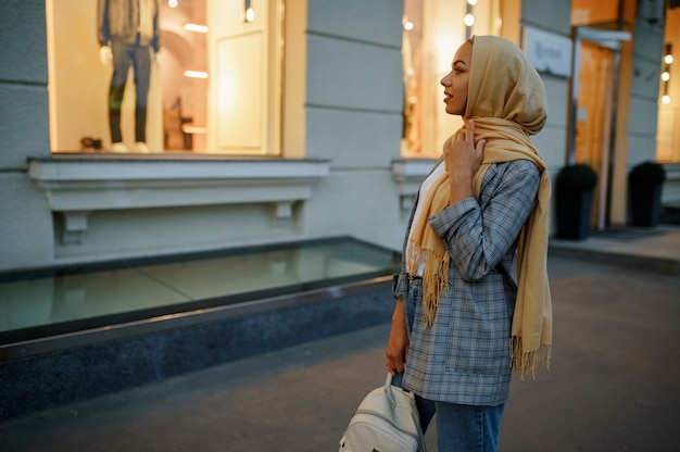 Chica árabe en hijab mirando el escaparate de la tienda de moda en el centro de la ciudad. Mujer musulmana caminando por la calle. F