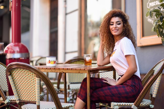 Chica árabe en ropa casual bebiendo un refresco en un bar al aire libre