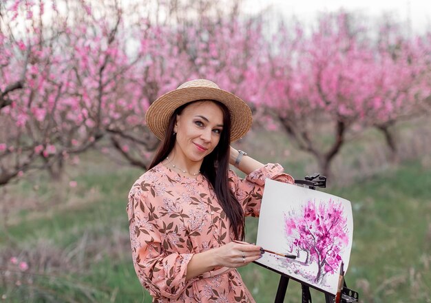 Chica artista pinta un huerto de duraznos en un manantial de huerto de duraznos