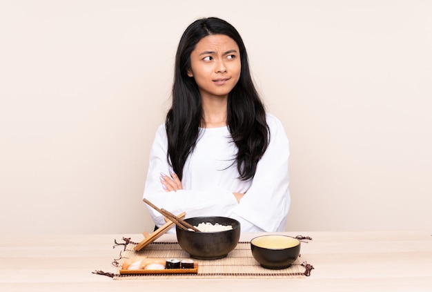 Chica asiática adolescente comiendo comida asiática aislada en beige