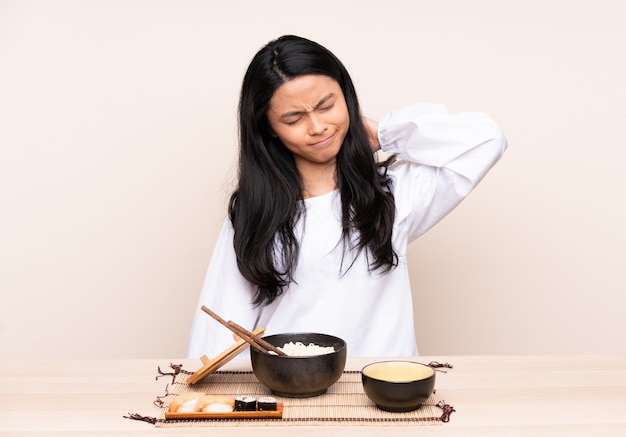 Chica asiática adolescente comiendo comida asiática aislada sobre fondo beige con dolor de cuello