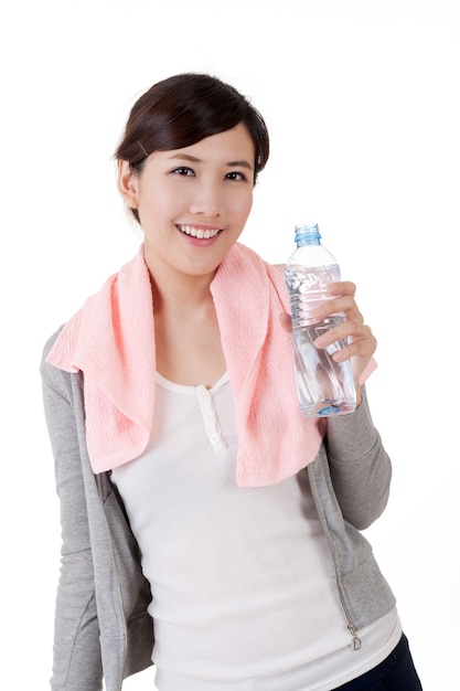 Chica asiática alegre sosteniendo una botella de agua, retrato de portarretrato con una toalla en el hombro sobre fondo blanco.