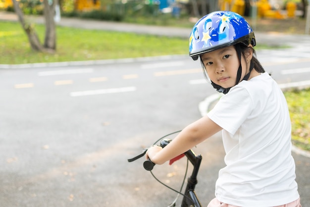 Chica asiática aprende a andar en bicicleta en el parque. Retrato de un niño lindo en bicicleta.