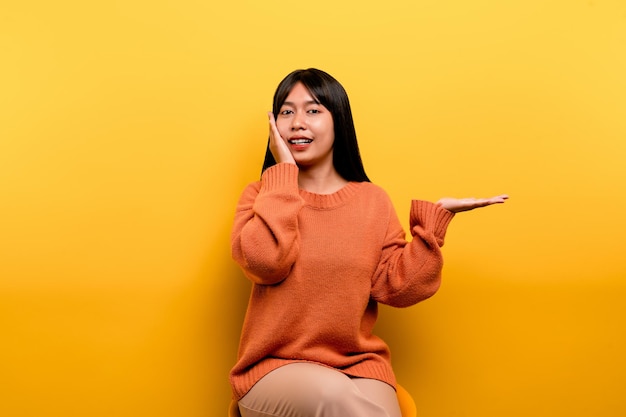 Chica asiática Bonita con un vestido casual naranja de fondo amarillo Celebra la victoria con una sonrisa feliz y la expresión del ganador con una expresión feliz de la mano levantada