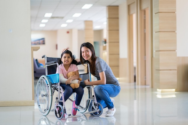 Chica asiática con un brazo roto con un ajuste de yeso en silla de ruedas con su madre en el hospital