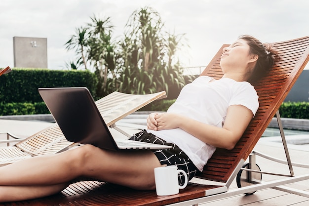 chica asiática en camiseta blanca trabajando con ordenador portátil y taza de café en pereza y relajarse pose