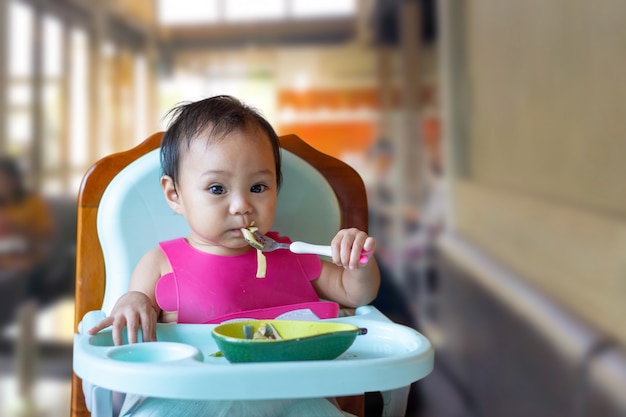 Chica asiática comiendo comida en la mesa del bebé.