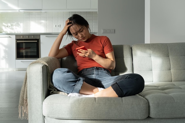 Una chica asiática deprimida y con el corazón roto leyendo un mensaje desagradable en un smartphone rompiéndose por teléfono