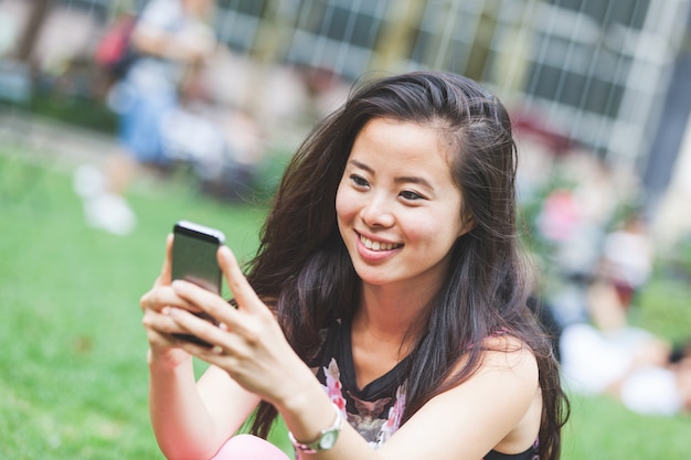 Chica asiática escribiendo en el teléfono inteligente en el parque