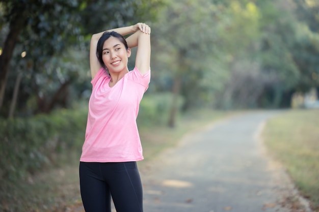Chica asiática está estirando los músculos calientes de su cuerpo antes de salir a correr al parque