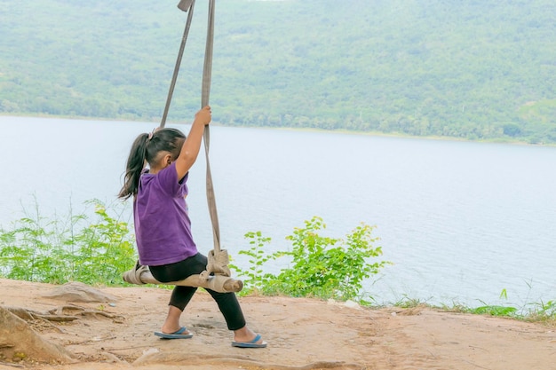 Una chica asiática está sentada en un columpio atado a un árbol detrás de un río de montaña