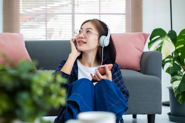 Chica asiática feliz con gafas escuchando música desde los auriculares en la sala de estar en casa Concepto de recreación en casa