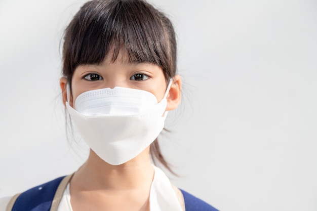 Chica asiática en el fondo blanco usa una mascarilla que protege contra la propagación de la enfermedad por coronavirus. Primer plano, de, un, niña, con, un, mascarilla quirúrgica, en, ella, cara
