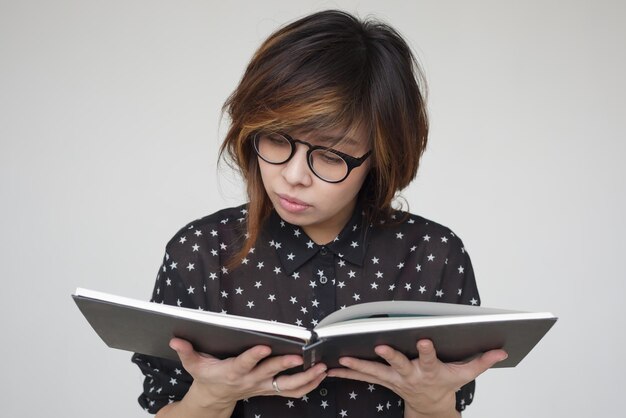 Chica asiática con gafas lee el libro cuidadosamente