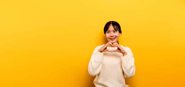 Chica asiática Hermosa con un vestido casual blanco sobre un fondo amarillo. Celebra la victoria con